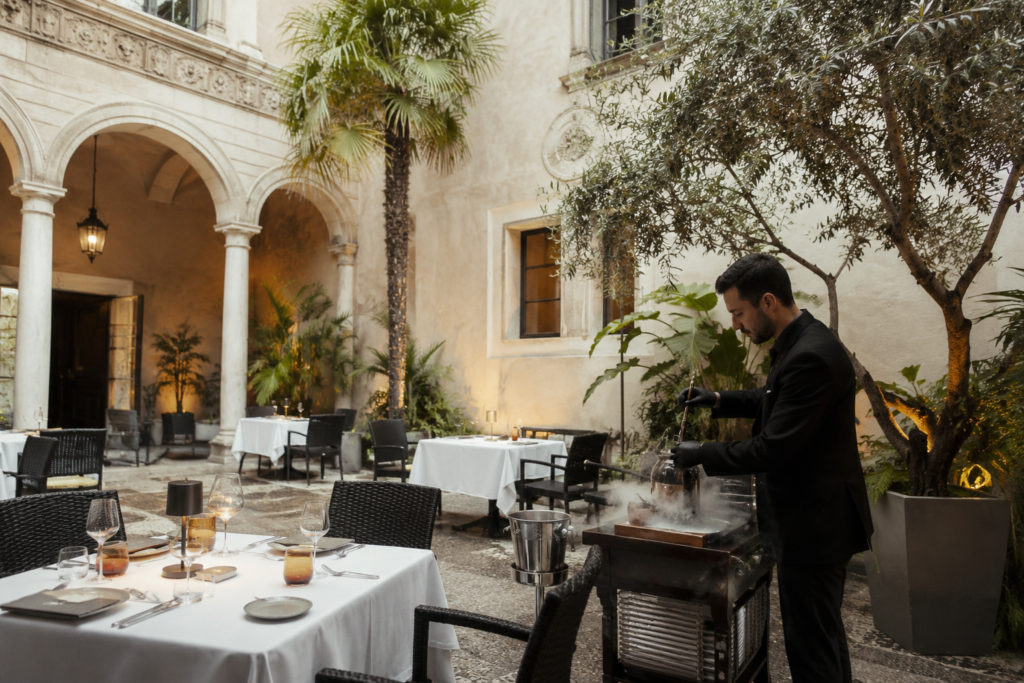Elegant courtyard dining experience at Balausta in Palacio Solecio Málaga with white tablecloths, arches, palm trees, and tableside service.