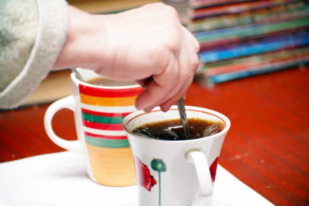 A woman stirs sugar with a teaspoon in a cup of tea