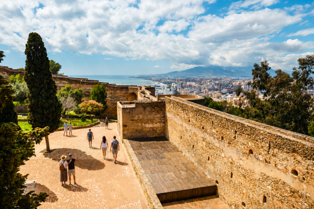 Blick auf die Alcazaba in Malaga mit Touristen, die spazieren gehen, und einem Paar, das Fotos macht und dabei die Stadt und die Küste überblickt.